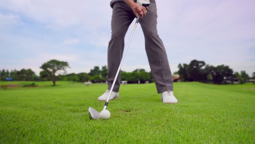 Close up of young male golfer swings his club on scenic golf course. Attractive sportsman enjoying outdoor recreation with light exercise and sport lifestyle while playing golf at course grounds.