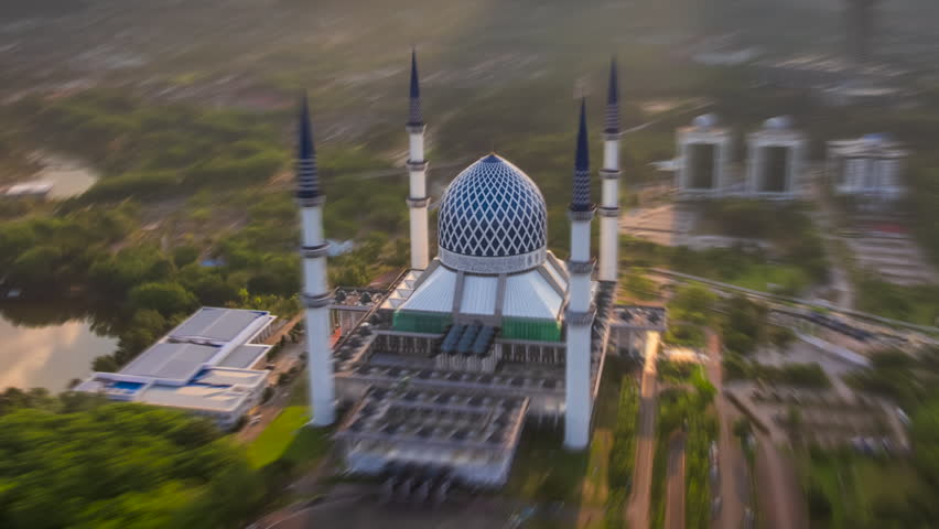 Sunset Ramadhan time lapse of golden landscape behind Shah Alam skyline in Malaysia with the Sultan Salahuddin Abdul Aziz Shah Mosque in the foreground. Zoom in motion timelapse.