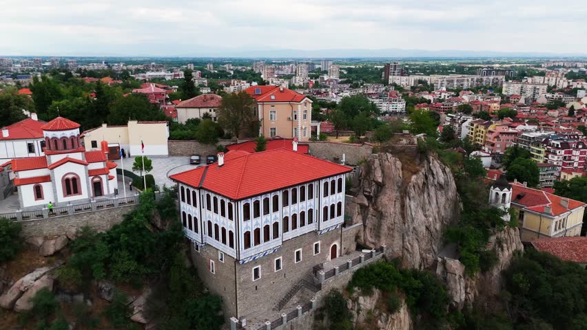 Slow aerial orbit of a grand Revival-era house museum perched on a cliff, overlooking Plovdiv’s historic landscape.