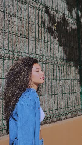 Profile view of a relaxed woman with long curly hair enjoying the sunshine outdoors