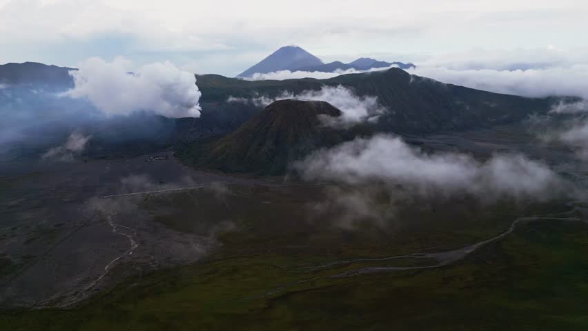 Aerial footage of the active Mount Bromo volcano releasing steam from its crater during gloomy weather. Thick clouds and muted light cover the caldera, highlighting the dramatic volcanic terrain.