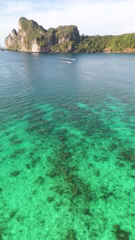 Drone camera pans over clear turquoise water toward tropical limestone karst islands in bright daylight