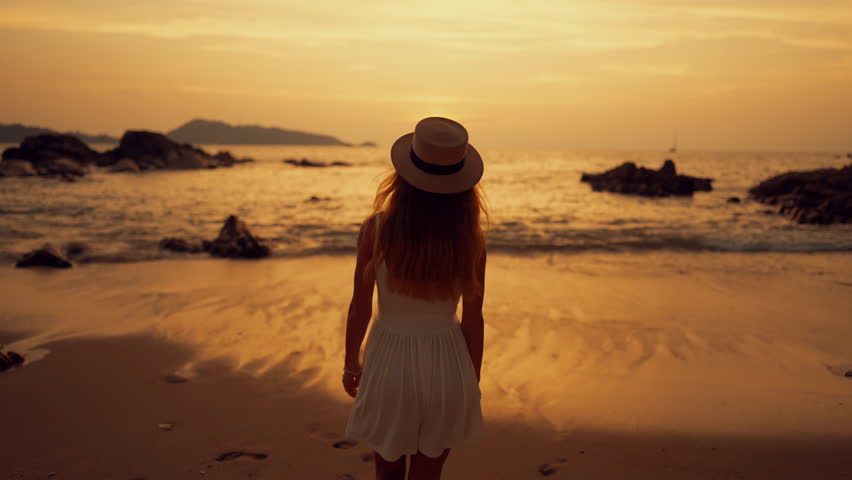 Beautiful woman and sea, back view of slender lady walking on beach in sunrise. Cinematic shot on ocean coast in early morning, woman admiring sunset above horizon, unity with nature and solitude