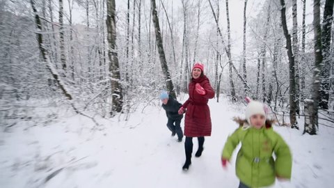 Mother with her kids hold hands and run in park at winter day