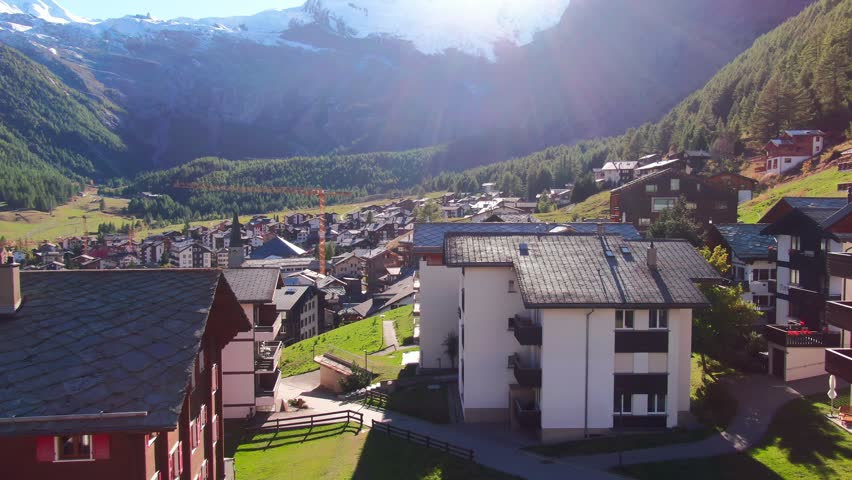 Golden sun rays over a traditional Swiss mountain village surrounded by alpine peaks and forests
