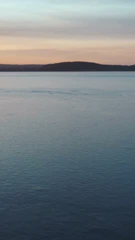 Static shot of a peaceful blue lake surface at sunset with distant hills on the horizon under colored sky.