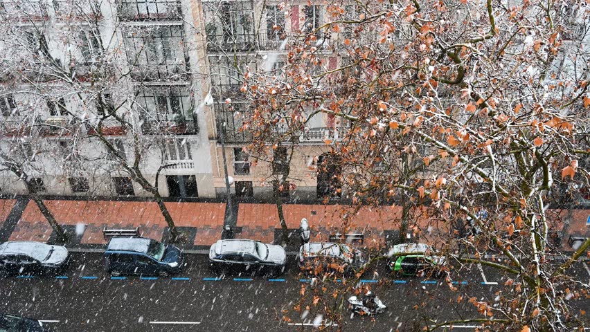 Madrid urban winter: High angle view of a residential street during a snowstorm. Large snowflakes fall in slow motion over parked cars and apartment balconies in Spain.