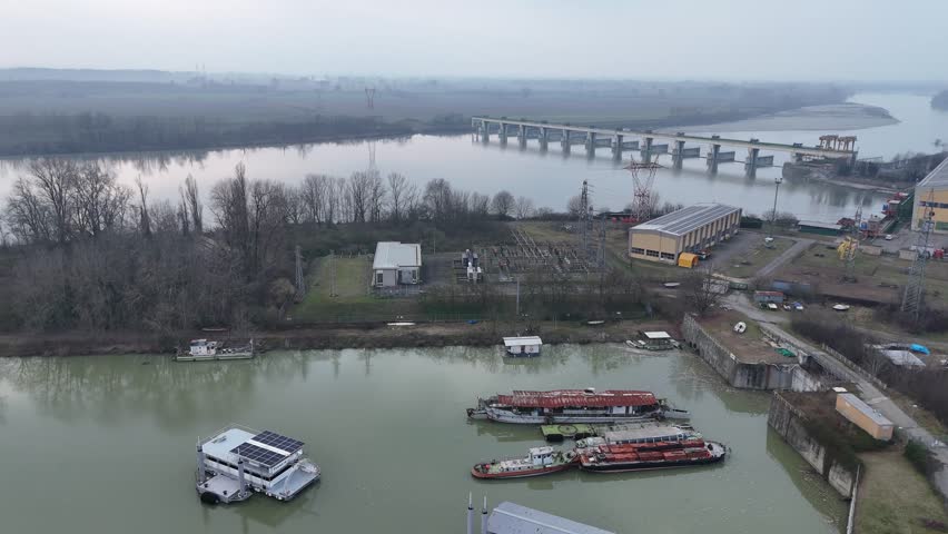 Inland harbor basin adjacent to the dam system, Multiple moored river barges and service vessels, Calm, sediment-rich Po River water, Diga di Isola Serafini, Monticelli d