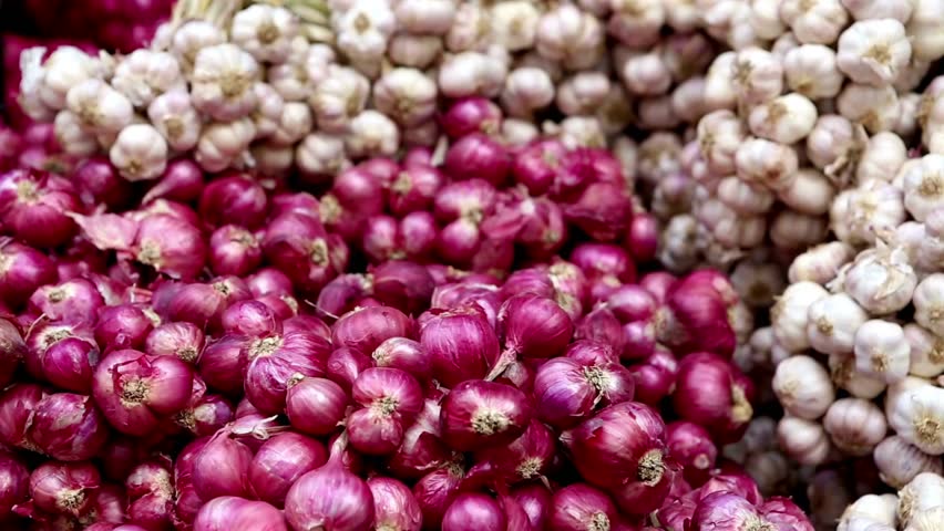 A large pile of fresh red onions surrounded by bunches of white garlic bulbs
