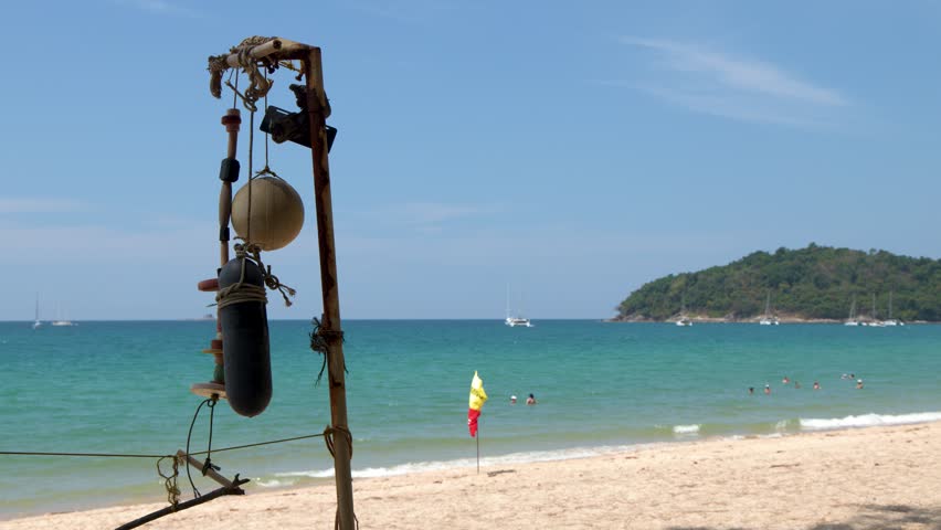 Static wide shot of a tropical beach with turquoise water, swimmers, and a rusted post