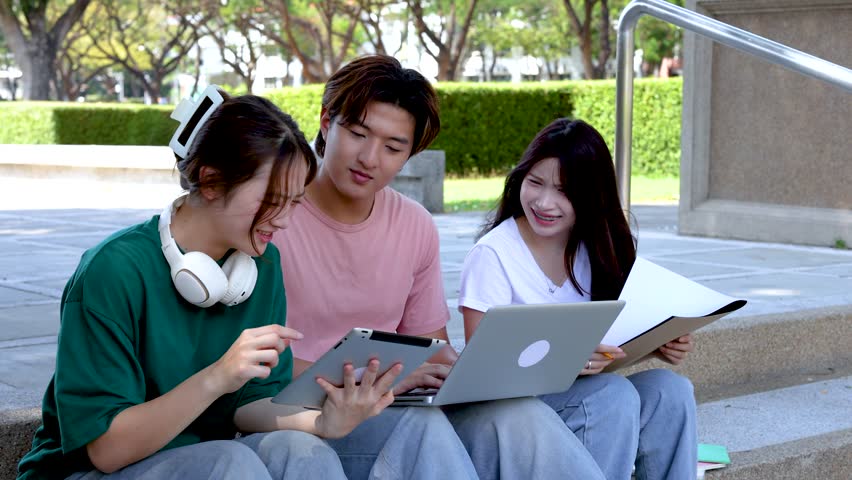 Diverse Asian students collaborate on a project using a laptop and tablet outdoors on campus