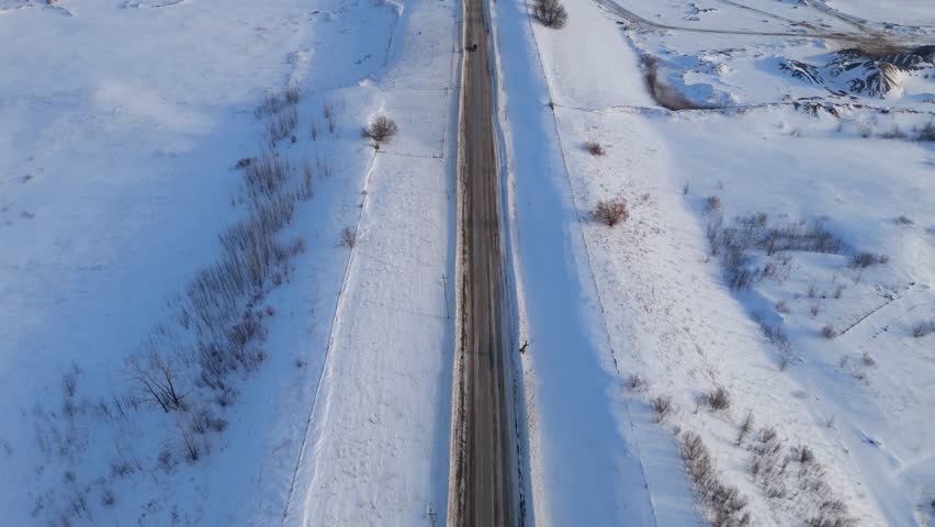 Aerial view of a car driving along a snowy road landscape during sunrise
