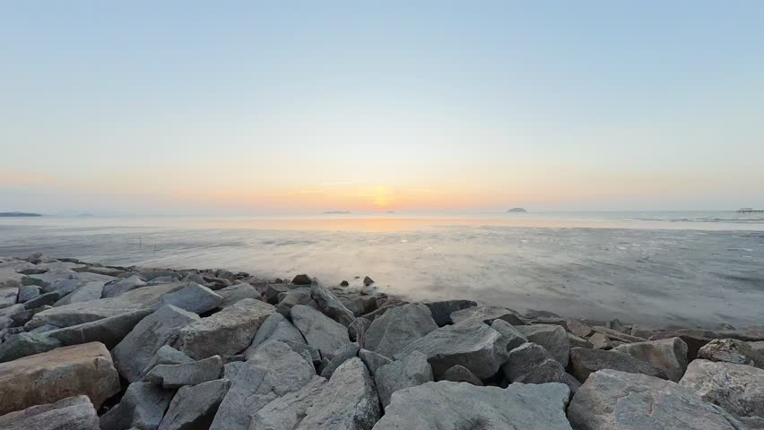 Soft sunrise over rocky shoreline and calm sea in Malaysia