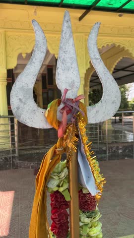 Close-up of a holy metal Trishul (trident) decorated with saffron cloth and garlands at a Hindu temple
