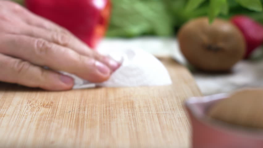 A man is cleaning the kitchen. His hands are wiping a large cutting board with a paper towel. They