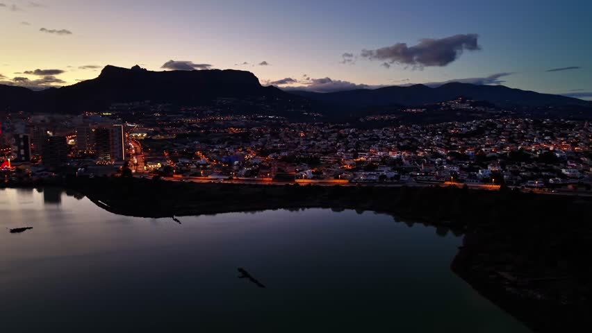 dusk skyline city with lights, twinkling urban lights reflected on calm lake, mountain silhouette framing