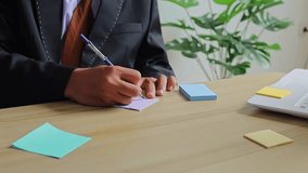 Professional businessman in black suit writes notes on purple sticky notes at wooden desk - Powered by Shutterstock - Get 15% off with code: PIKWIZARD15