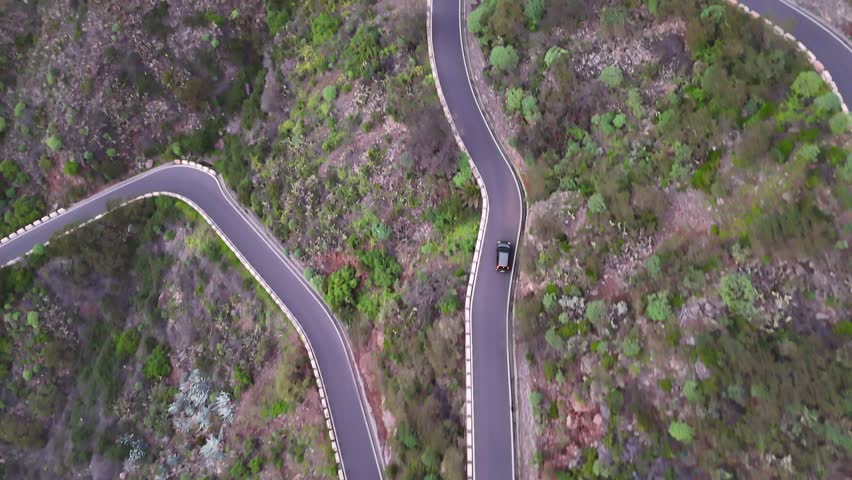 Aerial view of cars riding at winding mountain road, showcasing the scenic landscape with lush greenery and rocky terrain. Auto navigating through route curves during journey. Automobile trip