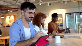Three young diverse professionals working together in a modern open plan office, using laptops and digital tablets while collaborating at a shared desk, highlighting teamwork and camaraderie - Powered by Shutterstock - Get 15% off with code: PIKWIZARD15