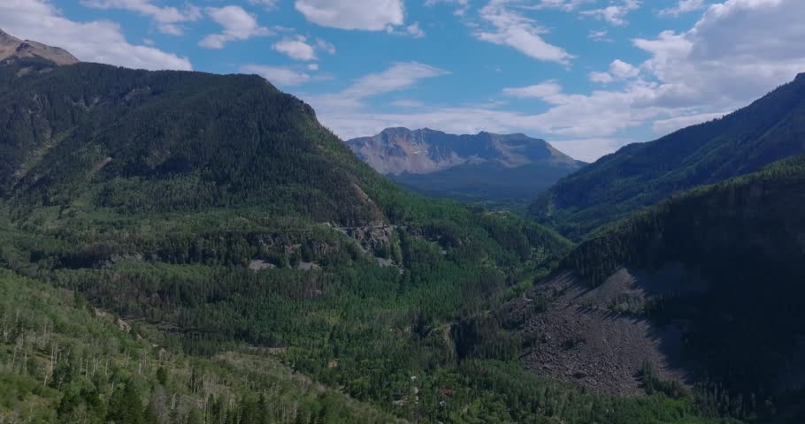 San Juan Mountain slopes surround Highway 145 as it follows the valley floor near Telluride, aerial overview