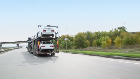 Carrier transports several cars by freeway at summer day, (view from car in motion)