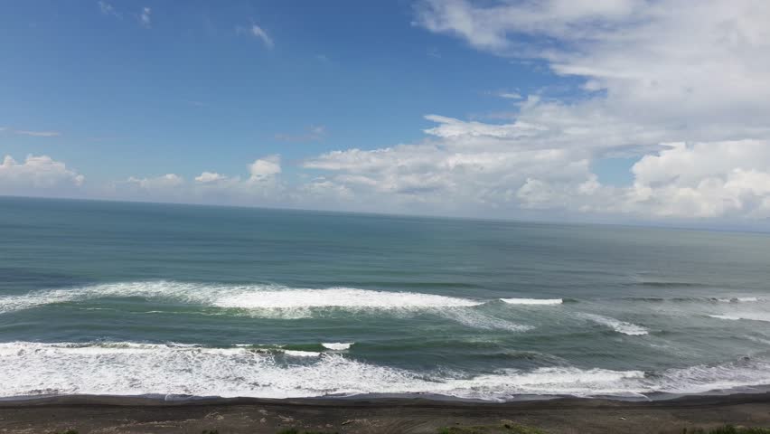 Aerial view of ocean waves breaking on the shore with lush green landscape