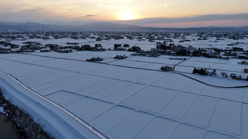 A snowy field with a sun setting in the background. The sky is a mix of blue and orange