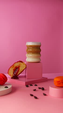 A hand lifts a foamy cappuccino from a sculptural pedestal, surrounded by a sliced Berliner donut, macarons, and photo props, perfect for lifestyle food branding and café product visuals.