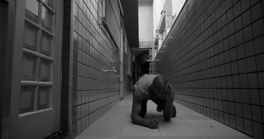 African American man kneels and leans forward in corridor, expressing collapse, hopelessness, emotional pain, and deep personal crisis