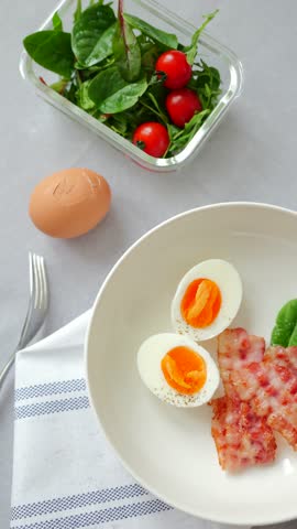 A breakfast plate shows hard boiled eggs with yellow yolks, bacon, spinach, and cherry tomatoes.