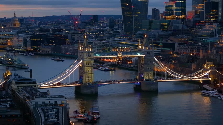 Aerial close-up view of the illuminated Tower Bridge of London with St. Pauls Cathedral in the background during dusk