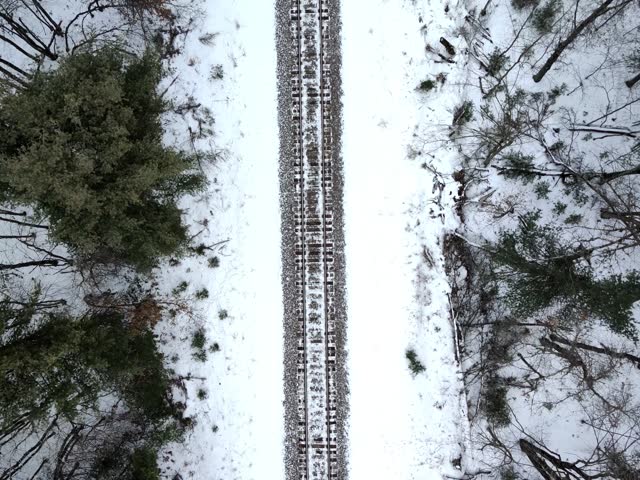 Aerial drone footage looking straight down at railroad tracks in a snowy winter landscape.