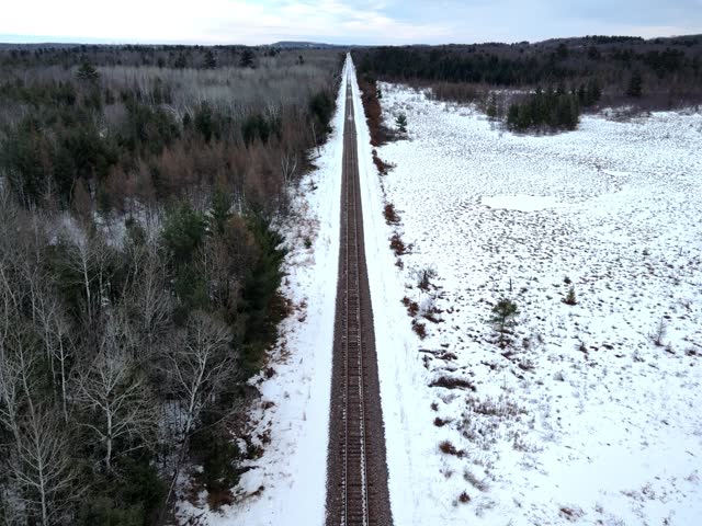 Aerial drone footage moving backward along railroad tracks in a snowy winter landscape.