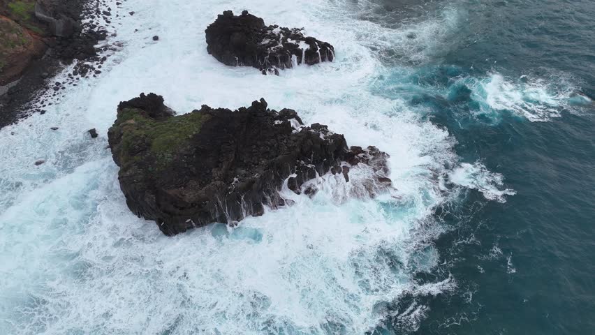 Aerial view of rocky coastline with crashing waves, showcasing the dynamic interaction between ocean water and rugged shore, highlighting the natural beauty of the coastal landscape