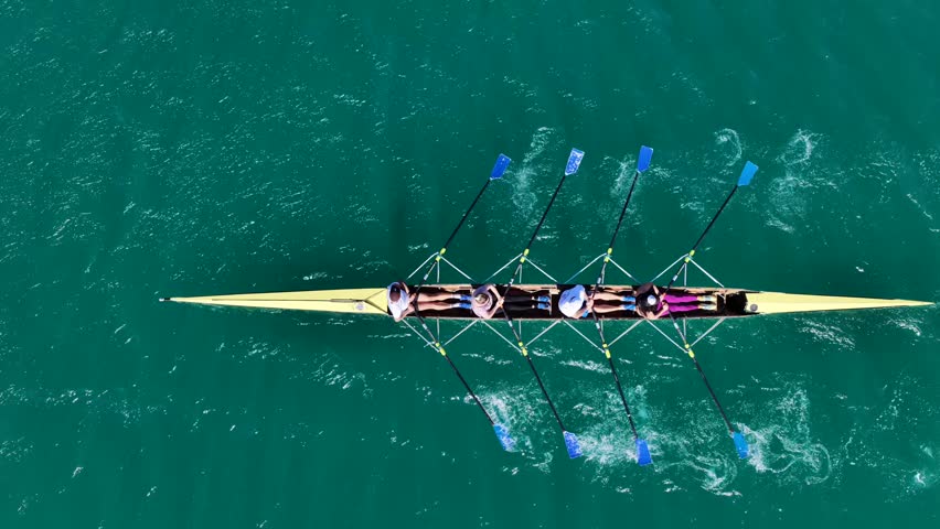 Aerial drone cinematic tracking video of team of athletes synchronous rowing in sport canoe in emerald calm lake