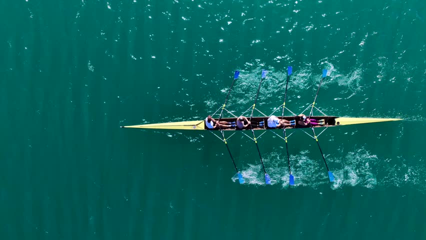 Aerial drone cinematic tracking video of team of athletes synchronous rowing in sport canoe in emerald calm lake