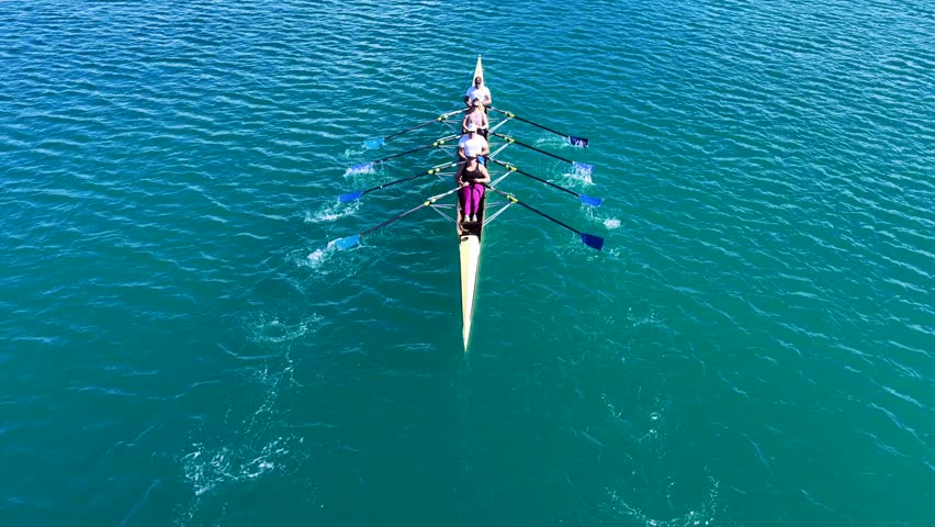 Aerial drone cinematic tracking video of team of athletes synchronous rowing in sport canoe in emerald calm lake
