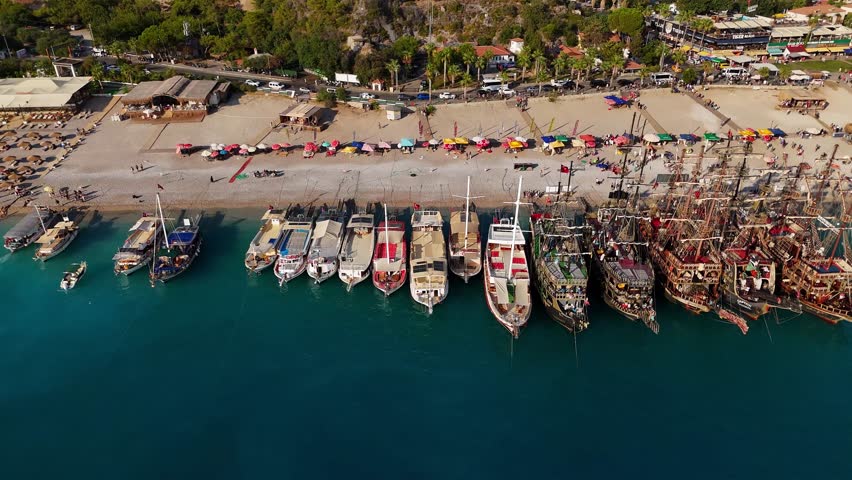 Drone aerial view of marina with tourist boats and pirate ships moored along a busy beach coastline on a sunny day. Pirate Ships