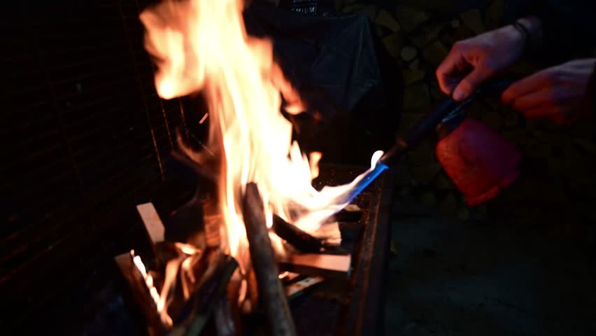 Person lighting a barbecue fire with a blowtorch at night