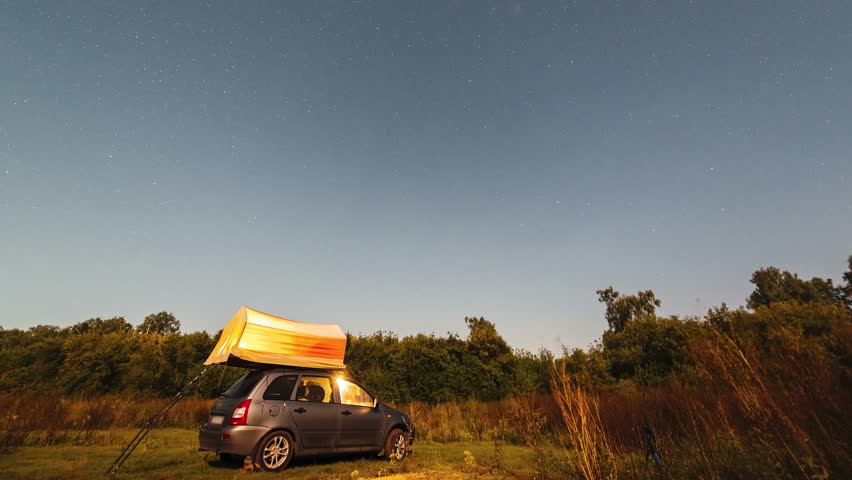 Timelapse, starry sky and Milky Way above a car and a tourist tent