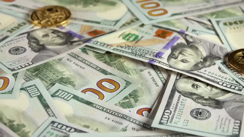 A detailed view of Bitcoin coins placed on a spread of US hundred dollar bills, highlighting the contrast between traditional and digital currency.