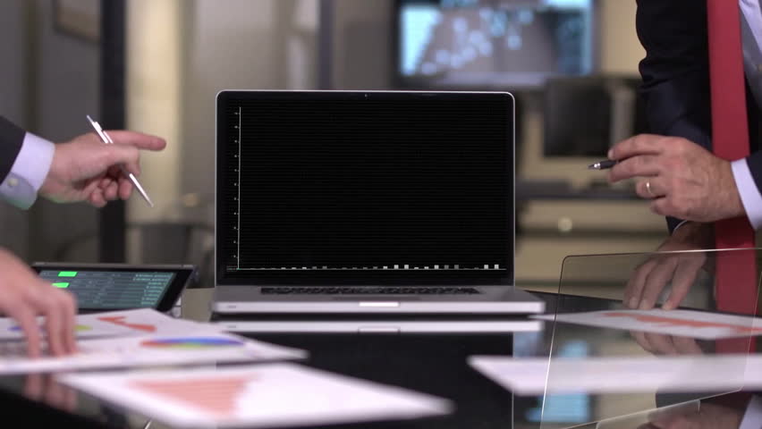 Two business professionals are reviewing financial charts and graphs displayed on a laptop screen in a modern office setting. The focus is on the data analysis process.