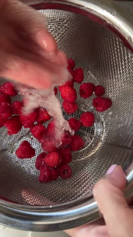 Fresh raspberries being washed in colander with water flowing and draining