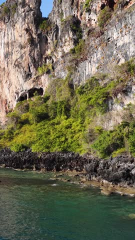 Drone pans across towering limestone cliffs and turquoise water under a clear blue sky