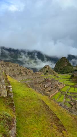 Machu Picchu panoramic view Inca trail tourist circuit terrances landscape sunny foggy clouds Peruvian Andes Peru Perú historic Inca Sanctuary Temple rainy season lush green jungle Vertical pan right