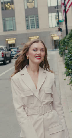 A beautiful smiling woman with red lips walks and posing confidently in front of massive building, in an uplifted mood.