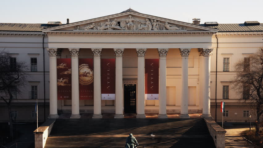 Front view of the Hungarian National Museum in Budapest featuring neoclassical columns and Roman exhibition banners, captured in daylight with historic architectural details.