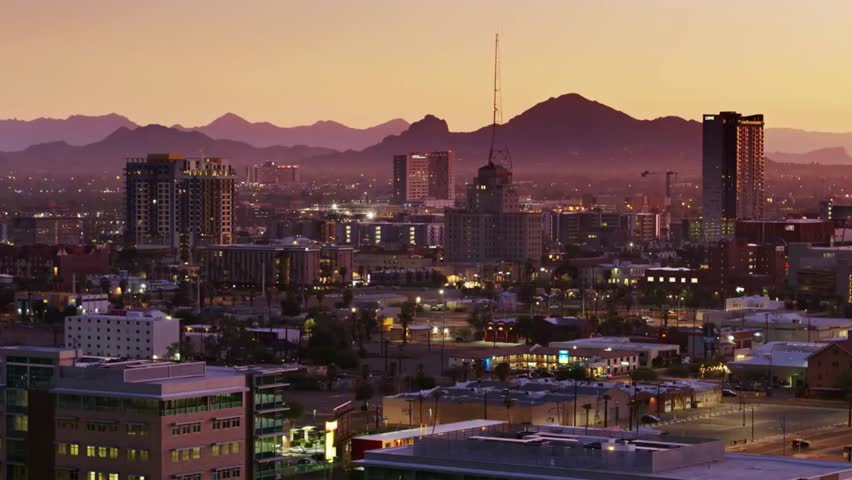 Phoenix skyline at dusk with mountains in the background under an orange sky, showcasing cityscape, sunset, and urban beauty.