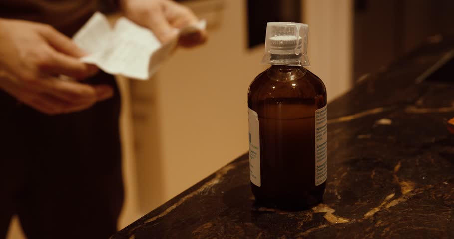 Medicine bottle on a kitchen counter while a person reads the package leaflet. Concept of medication safety, correct usage, dosage instructions, and healthcare awareness.