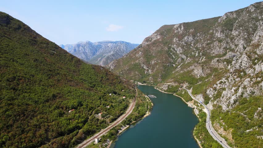 Aerial drone view flying above the Neretva River canyon with mountain road and railway following the turquoise water through steep rocky cliffs in Bosnia and Herzegovina.